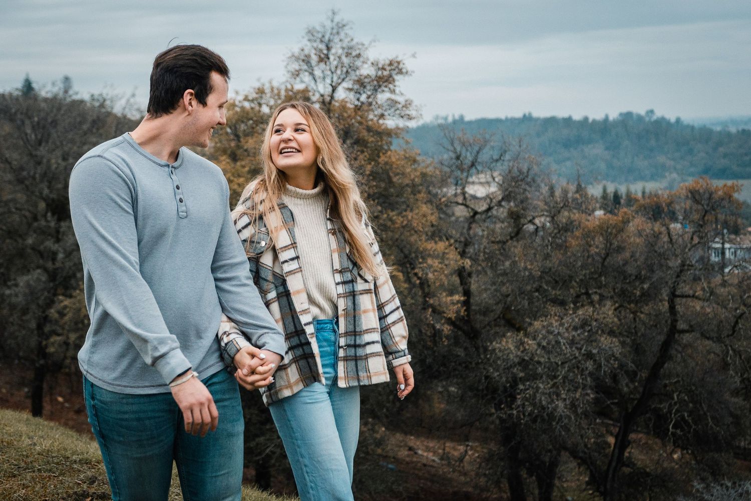Couple sharing a laugh while holding hands on an autumn hillside.