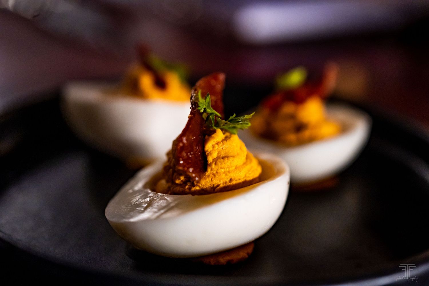Close-up macro photography of deviled eggs garnished with herbs on dark background.