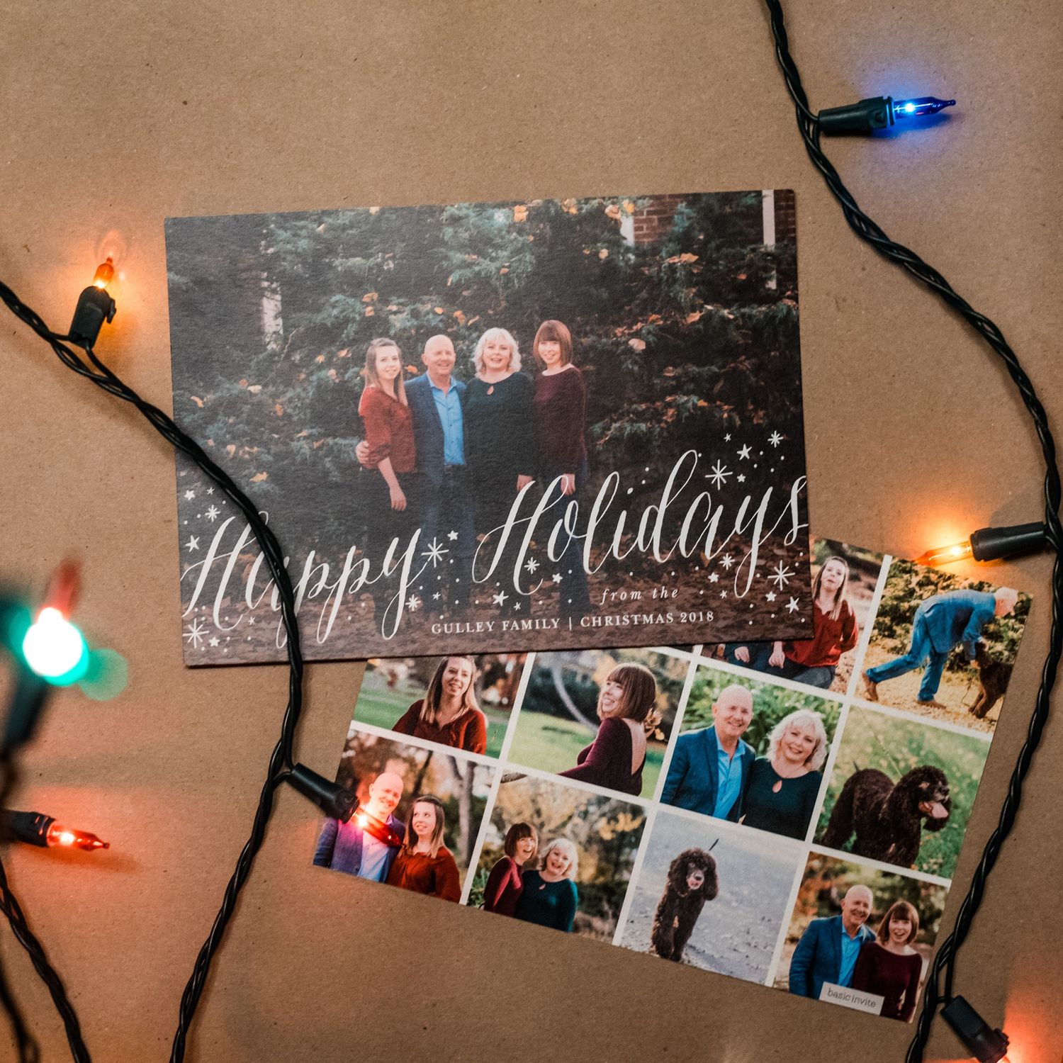 Holiday greeting cards with family photos surrounded by festive colored string lights on a brown surface.