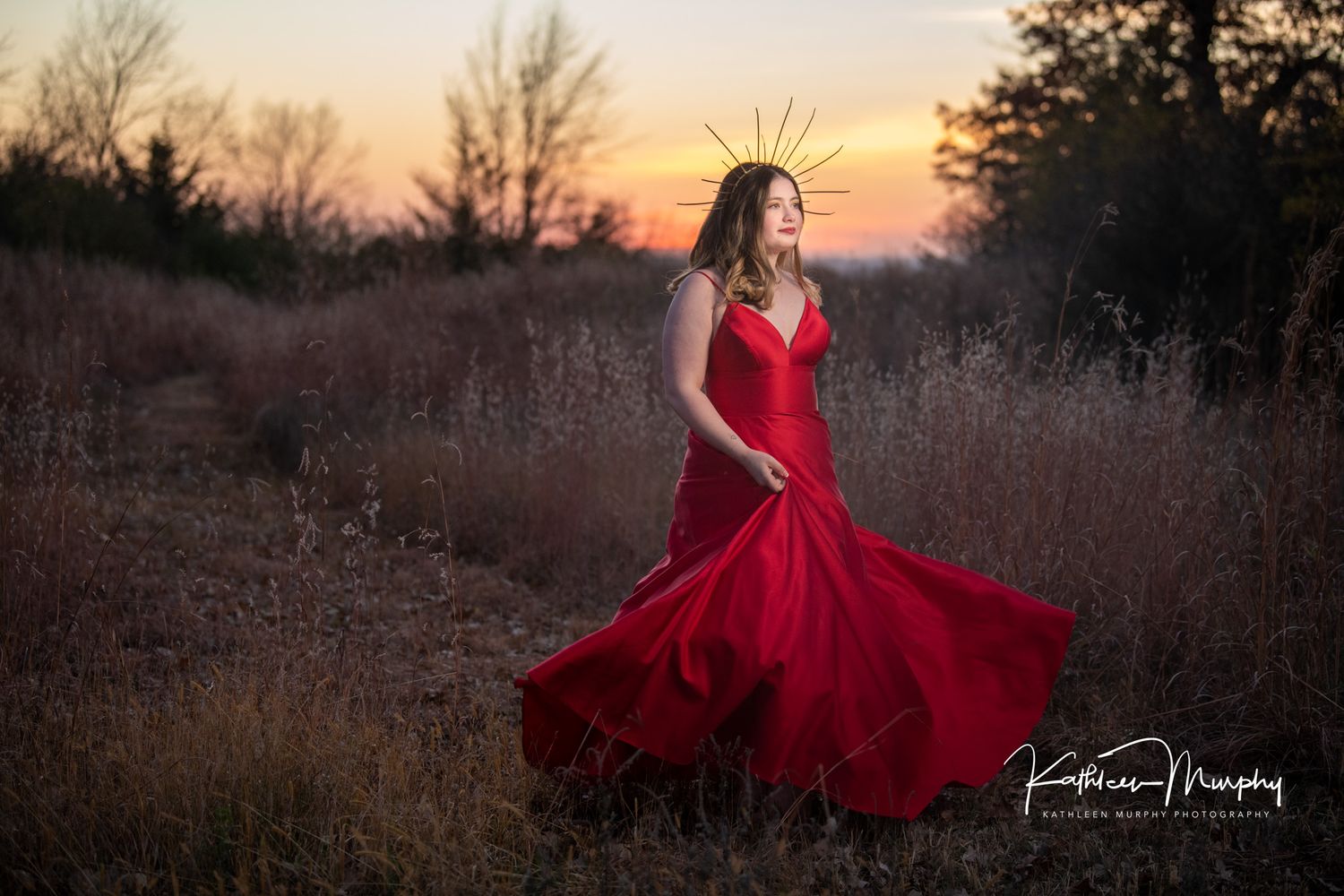 Red flowing dress twirling in golden sunset light among tall grass.