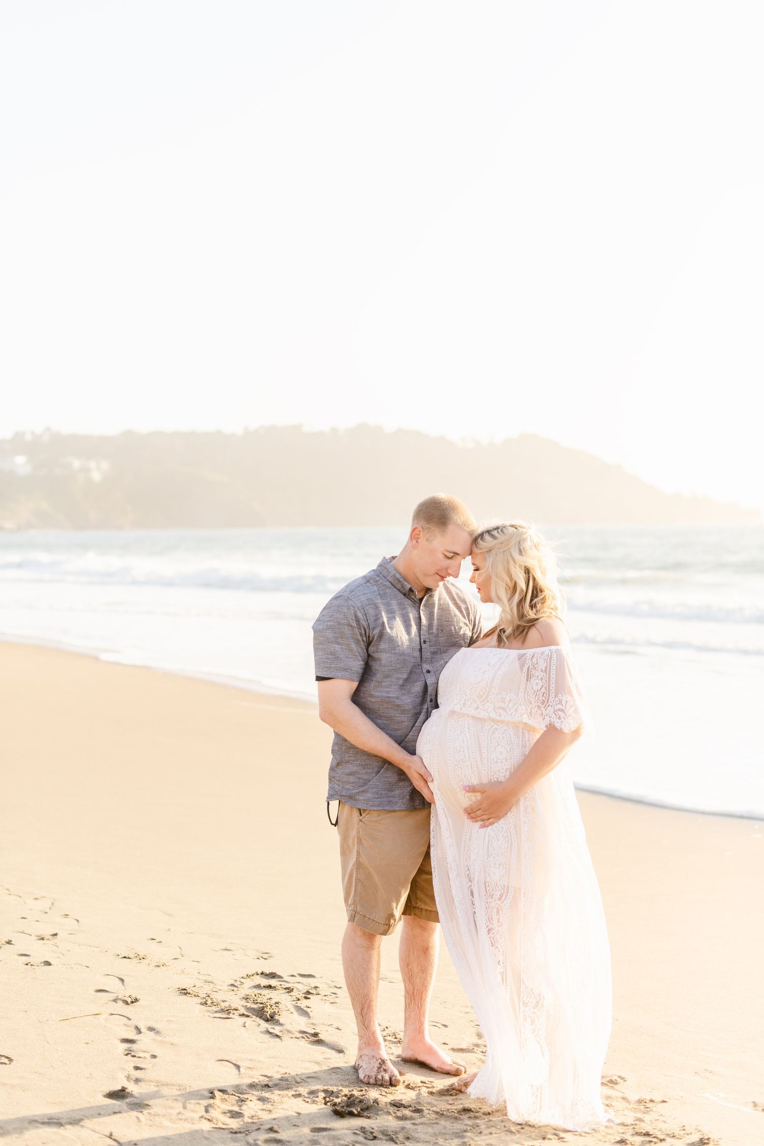 A romantic beach photography session with a couple embracing on a sandy shoreline at sunset.