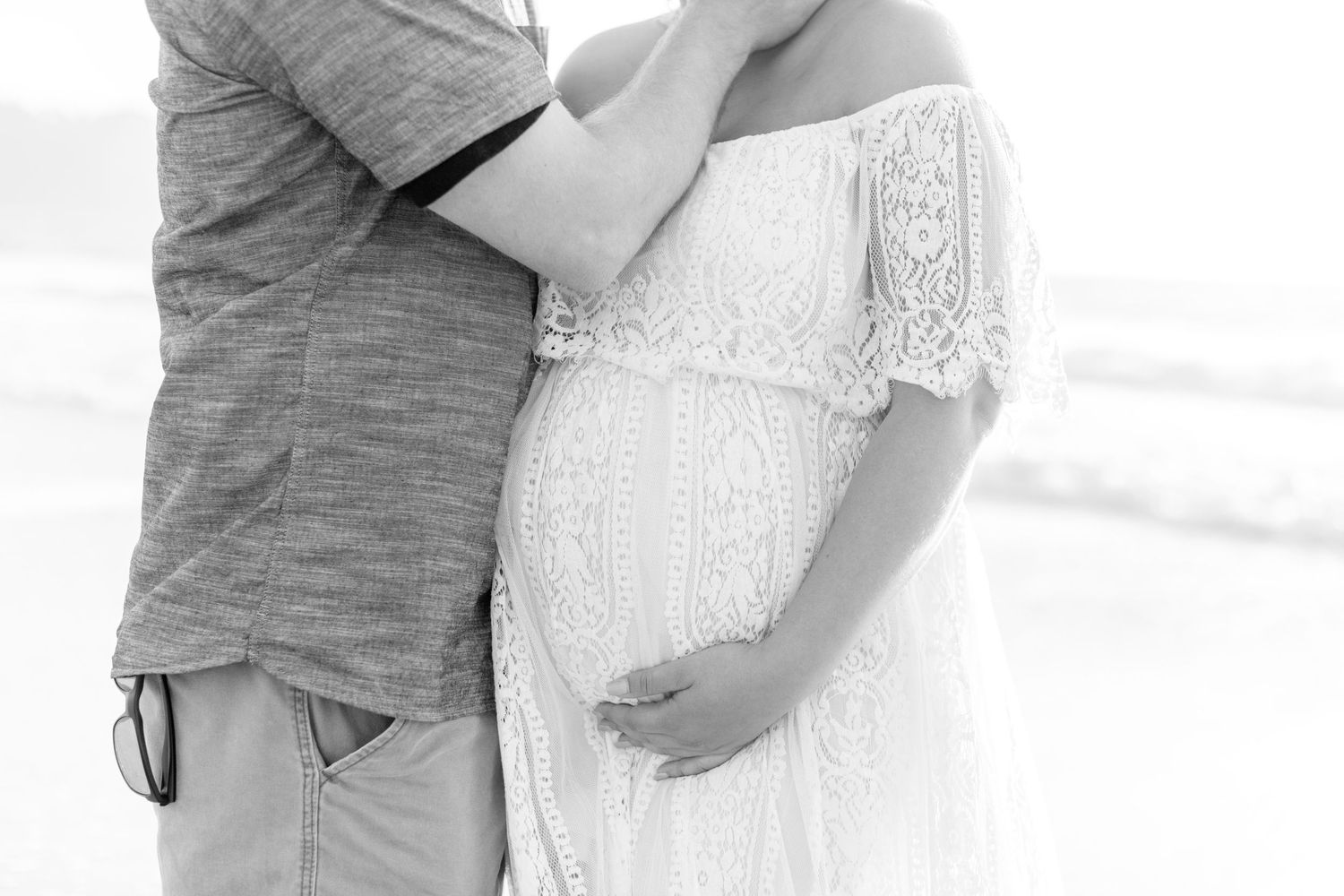 Black and white maternity photo showing couple embracing on beach.