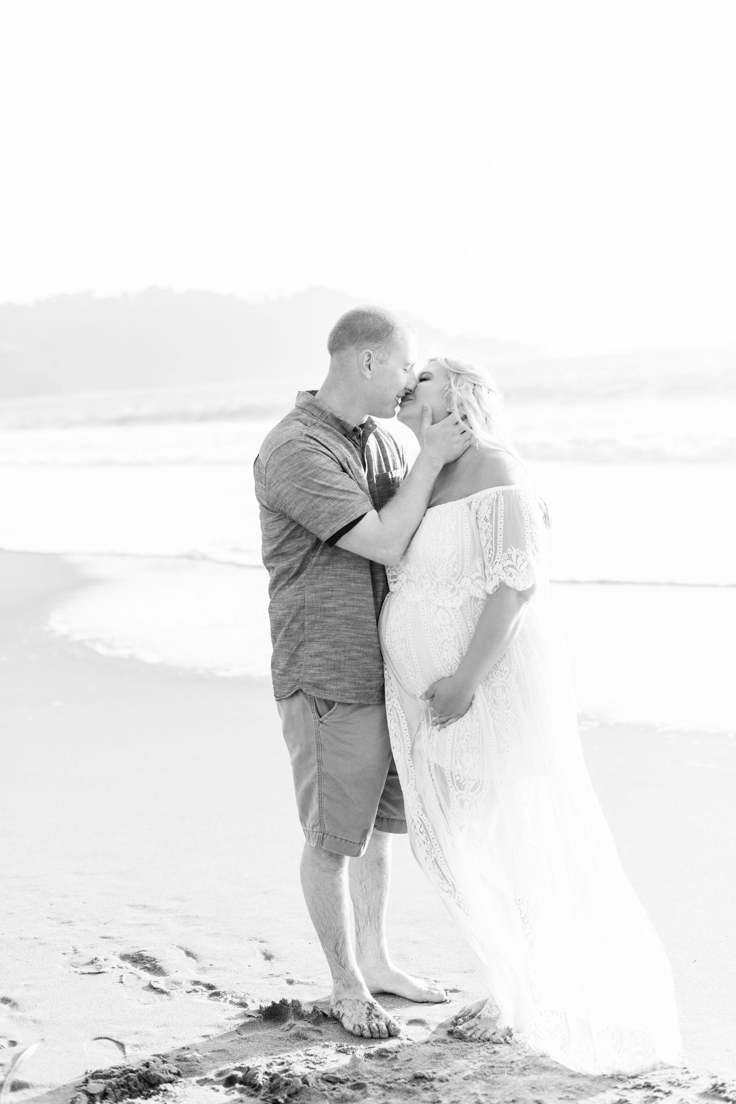 High-key beach portraits showing tender embraces between a couple on the sand.