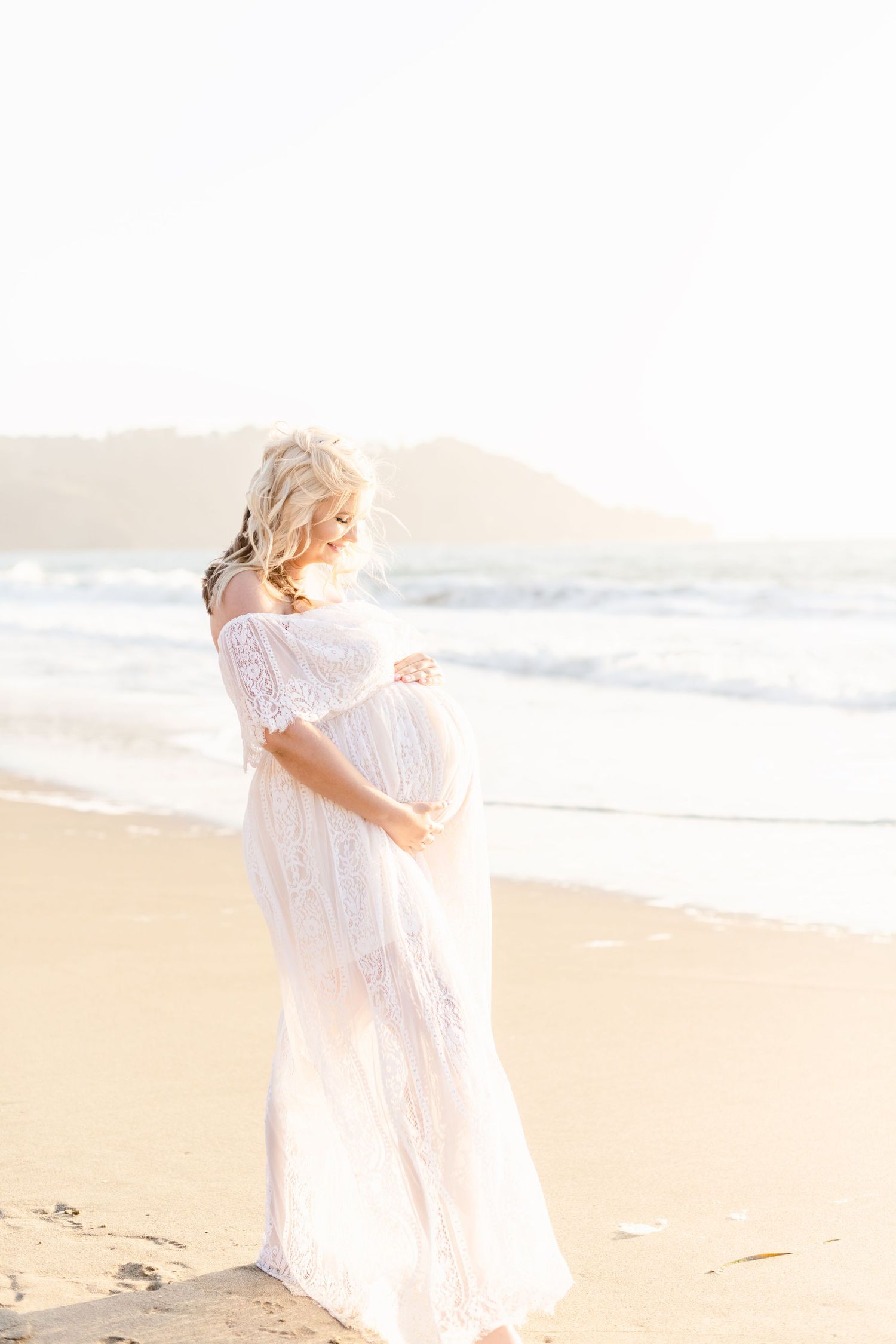Sun-drenched beach portraits featuring ethereal white lace dress against ocean backdrop.