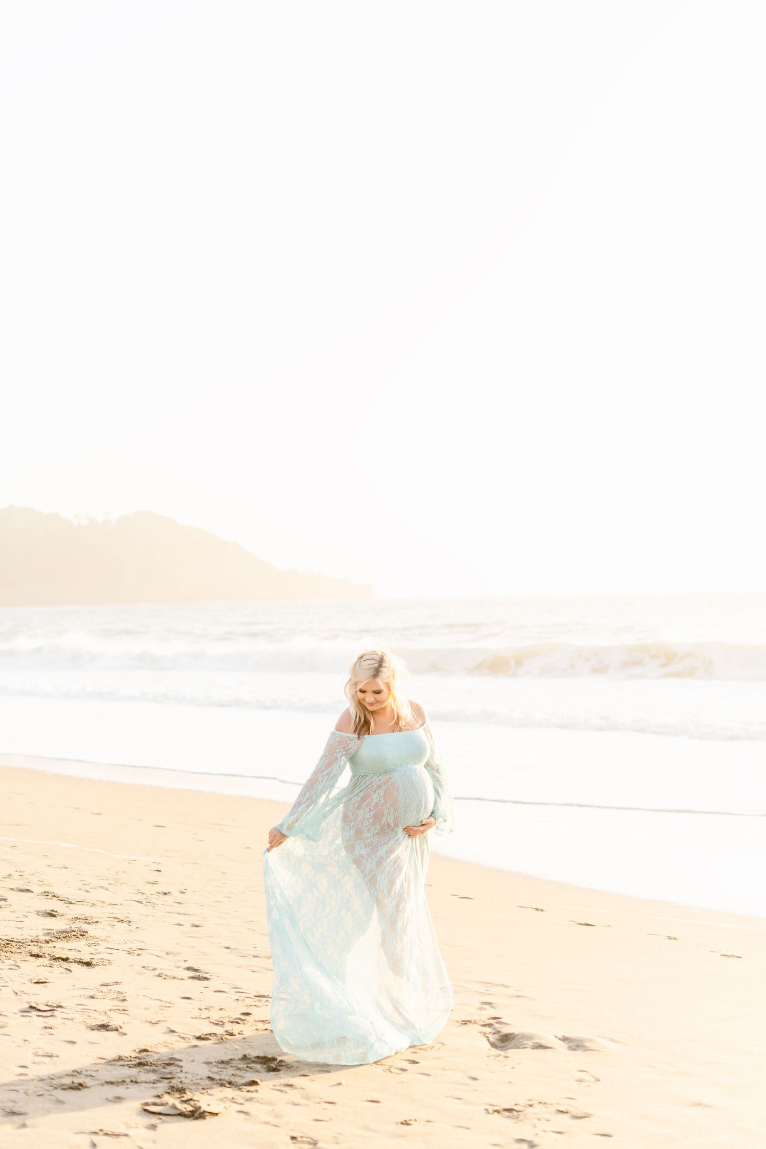 Woman in flowing dress twirls on sandy beach at sunset.