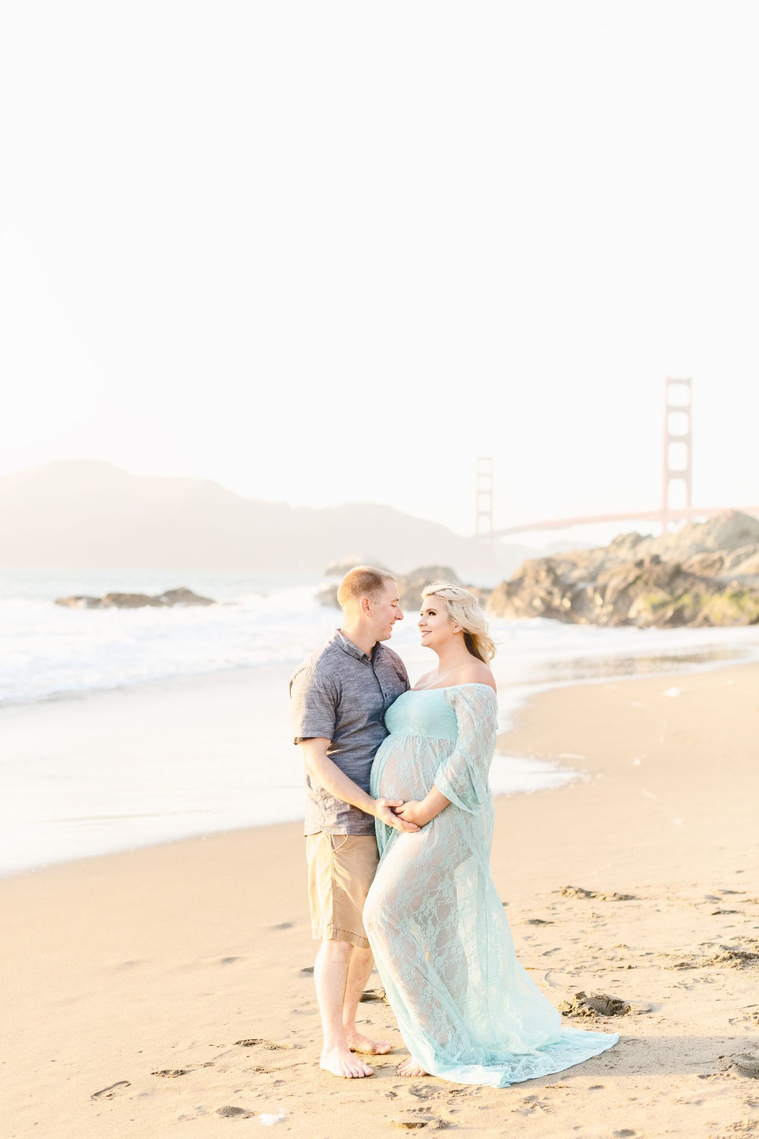 Couple shares intimate moment on beach with San Francisco landmarks in background.
