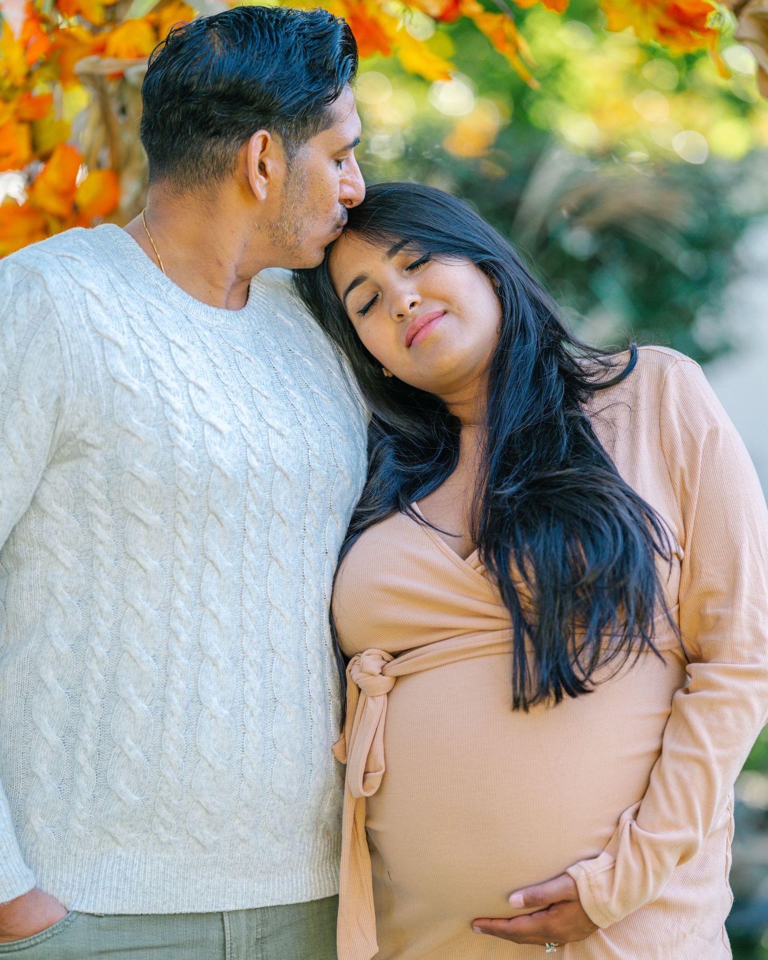 A couple shares an intimate moment during their maternity photoshoot surrounded by fall colors.
