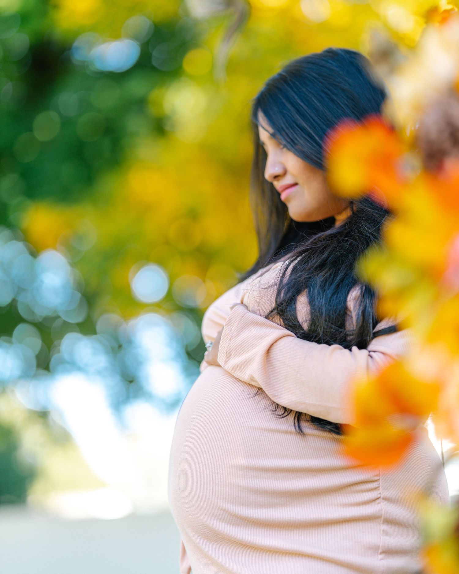A maternity photoshoot in a park with autumn foliage and bokeh lighting effects in the background.