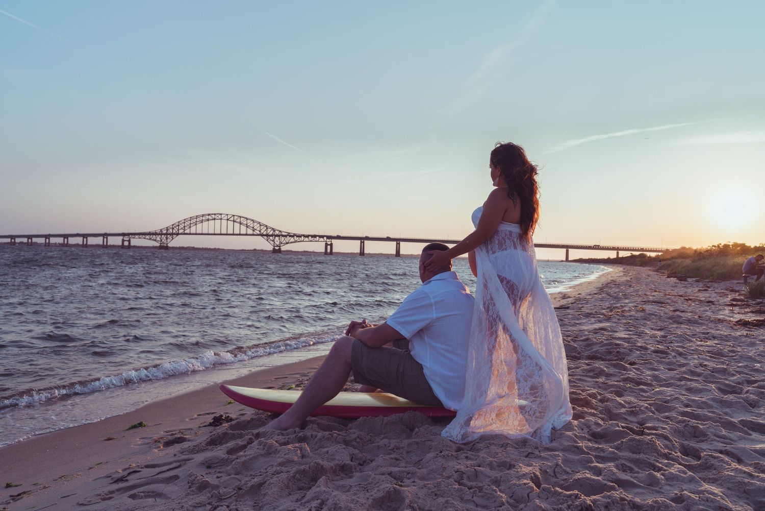 Romantic beach scene with bridge silhouette during golden hour.