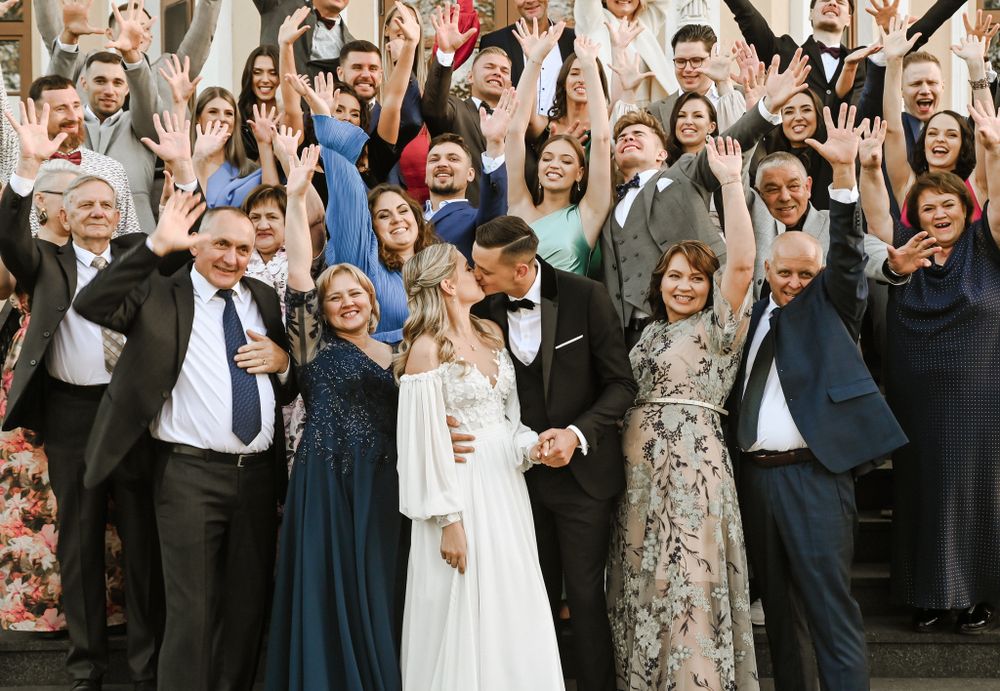 Large wedding group photo with excited guests celebrating and raising their hands in unison.