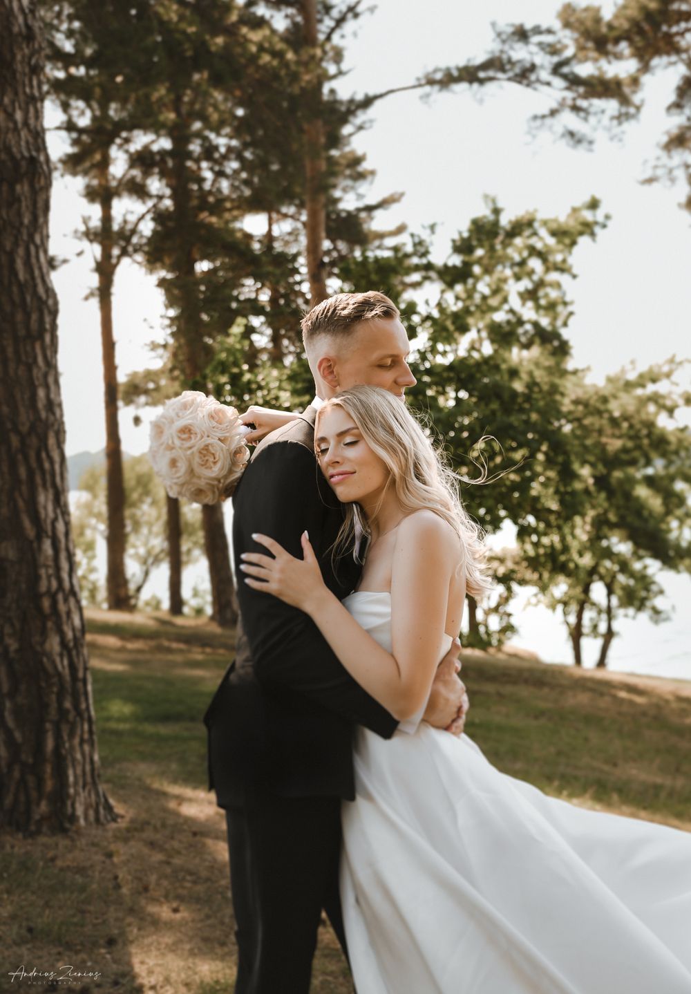 A tender wedding embrace photographed in a scenic pine forest setting.