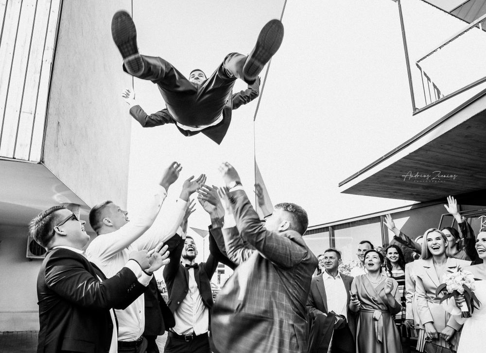 Wedding guests toss and catch someone in the air during an energetic celebration.