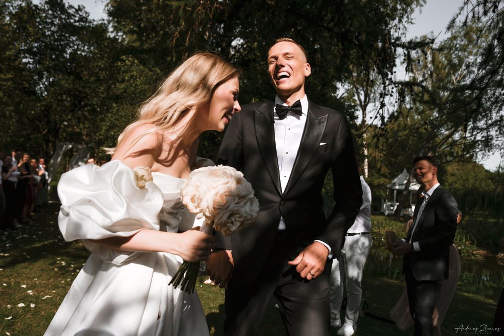 Couple sharing joyful moments during an outdoor wedding celebration near trees.