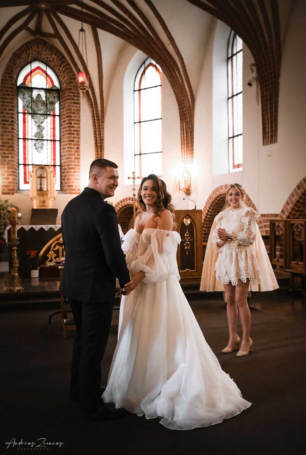 Wedding ceremony in a beautiful gothic church with brick walls and stained glass windows.