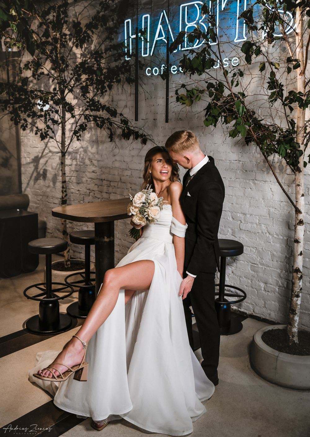 Stylish wedding couple poses intimately at modern cafe with neon signage.