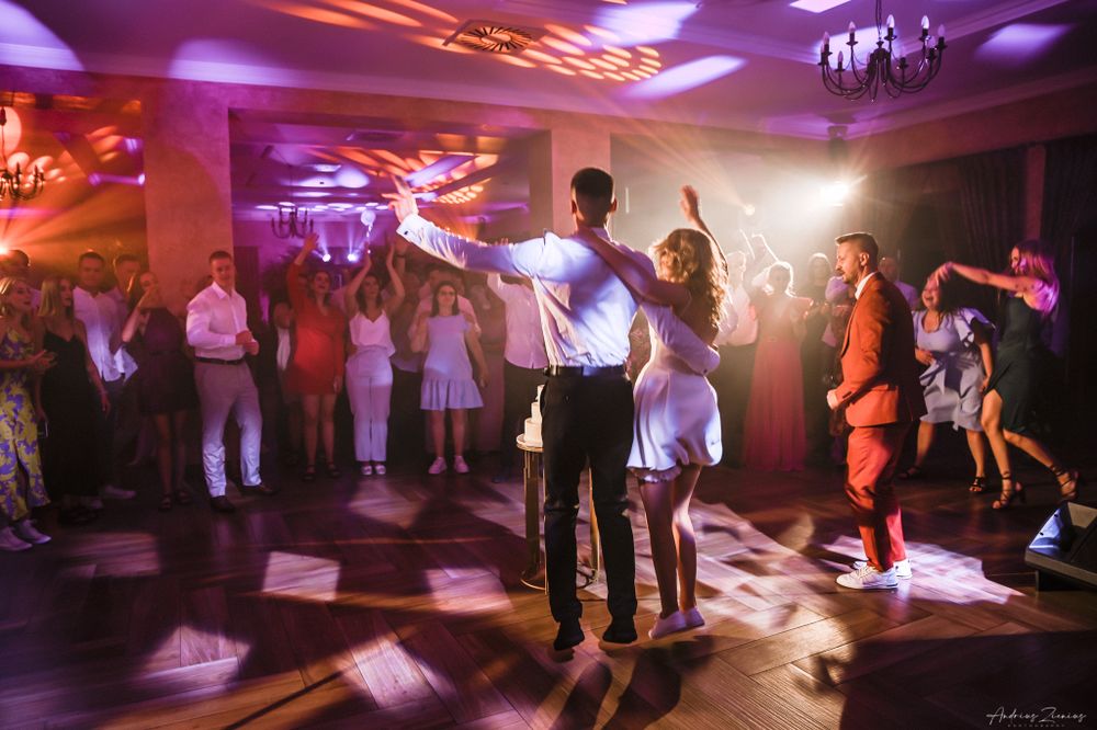 Wedding reception dance floor illuminated with purple lights as guests dance in celebration.