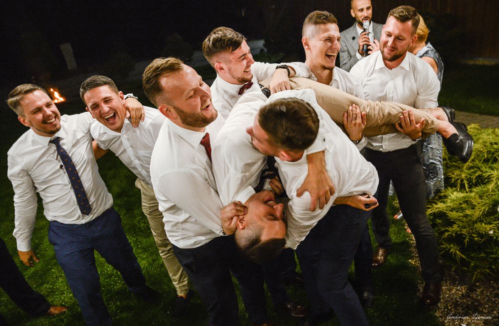 Groomsmen in white shirts playfully pose together on grass during wedding celebrations.