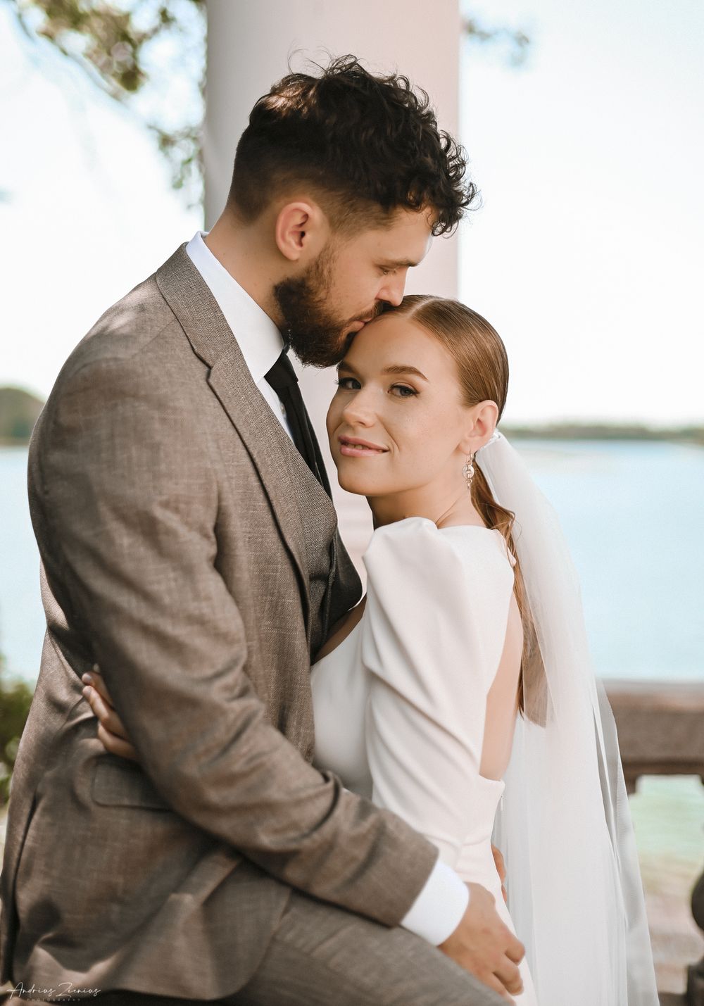 An intimate portrait of newlyweds sharing a tender moment against a waterfront backdrop.