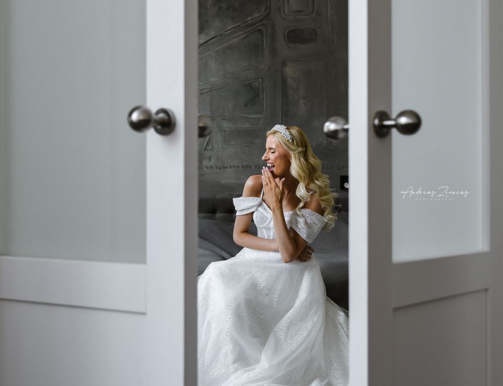 Bride in white gown sits elegantly framed between double doors.
