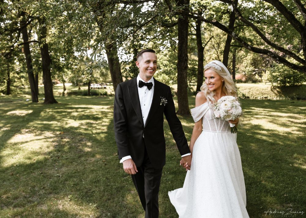 Couple walks hand in hand through sunlit garden in wedding attire.