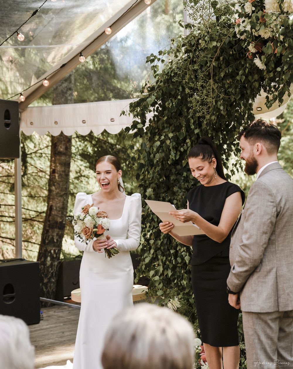 A wedding ceremony under a clear tent with greenery and natural decor.