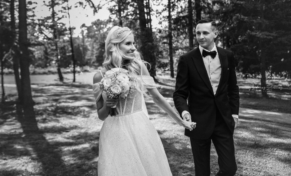 Wedding couple walks hand in hand through sunlit forest path.
