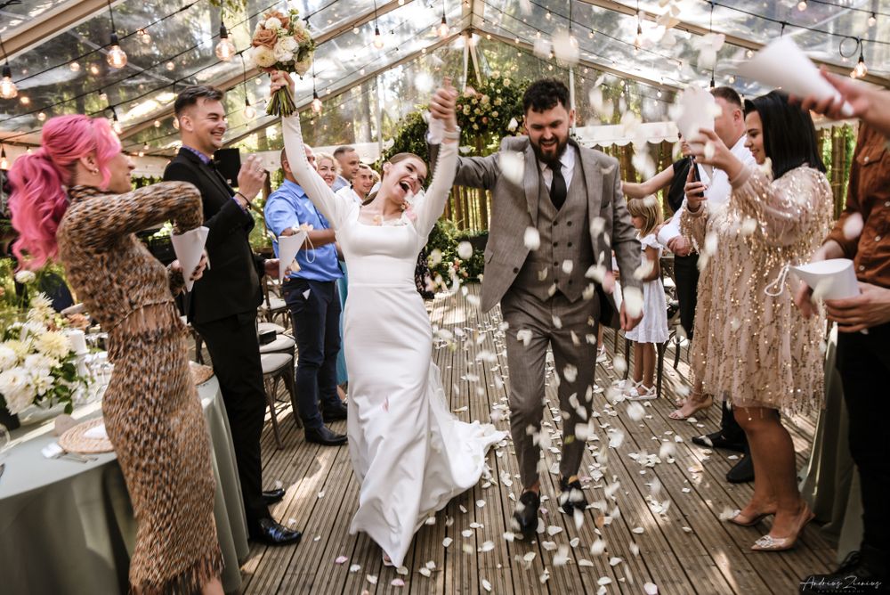 Wedding party celebrating with confetti as newlyweds exit their greenhouse reception venue.