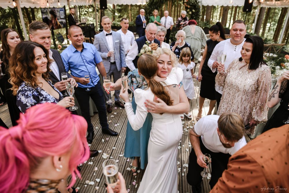 Wedding guests celebrate on a wooden deck during an outdoor reception in the woods.