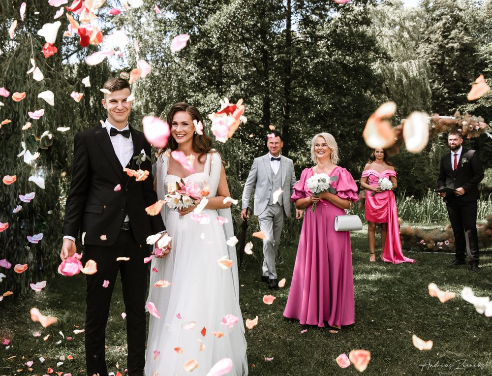 Wedding party celebrates with flower petals being tossed in a lush garden setting.
