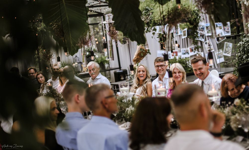 Atmospheric wedding reception scene with guests mingling under string lights and greenery.