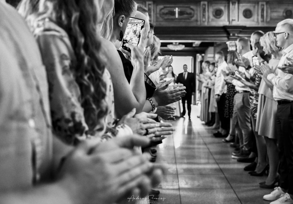 Wedding guests line a corridor holding phones to capture a special moment in black and white.
