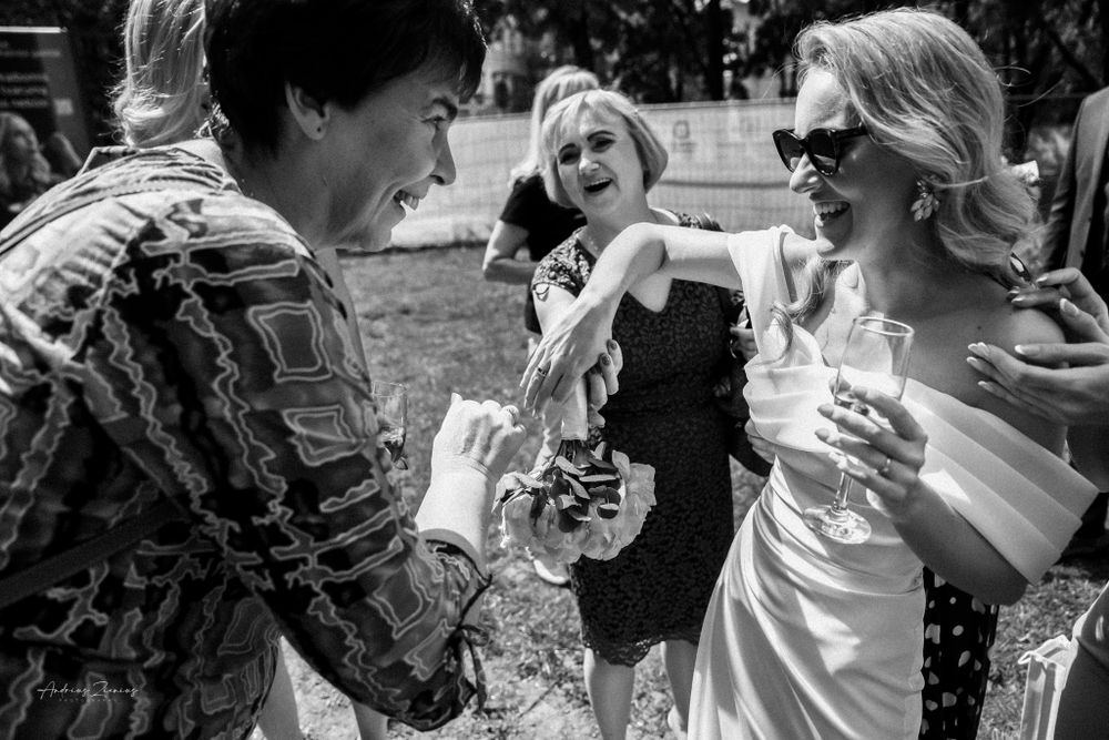 Candid black and white photo of guests laughing and enjoying drinks at an outdoor reception.