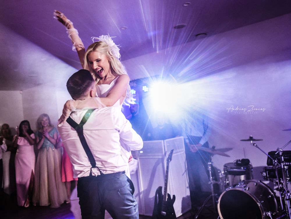 A newlywed couple dances together during their reception under purple stage lighting.