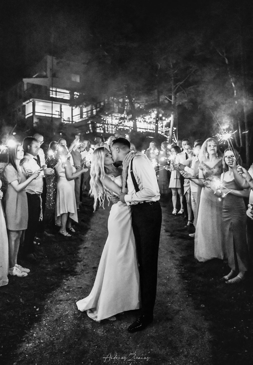 Wedding reception guests dance under twinkling lights in elegant black and white photography.