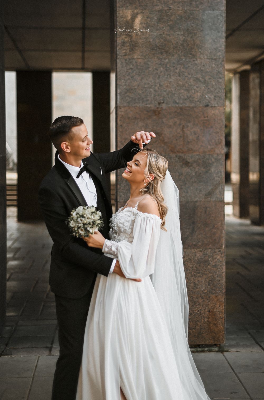 Elegant couple dancing in an industrial venue with stone columns and white wedding attire.