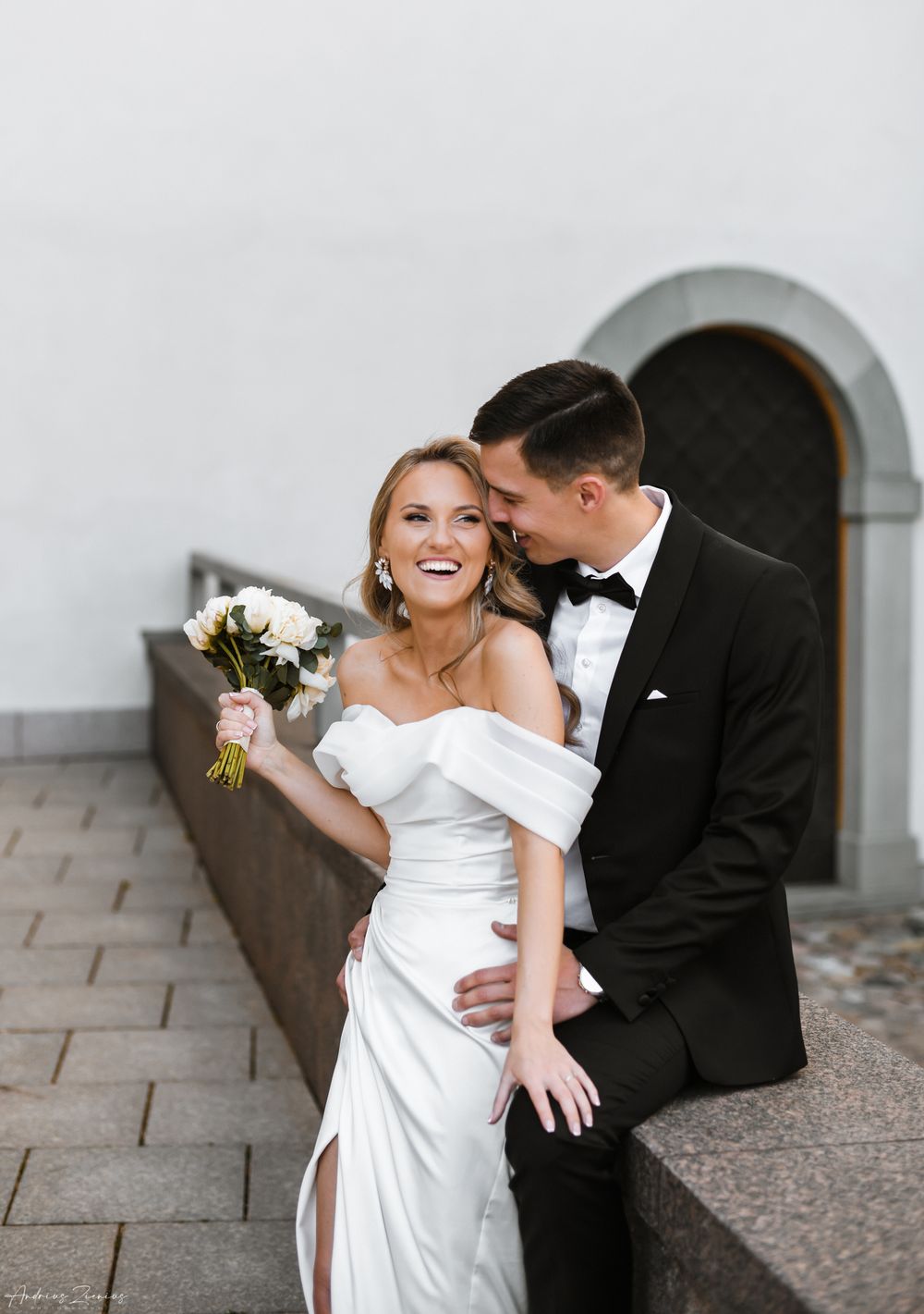 Elegant couple in formal wedding attire sharing an intimate moment against a stone wall.