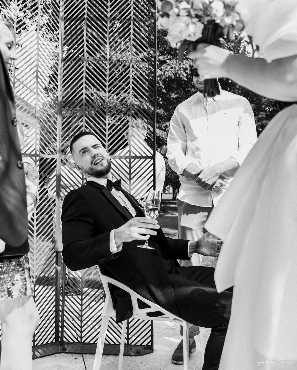 Black and white photo of groom relaxing in formal attire during wedding reception.