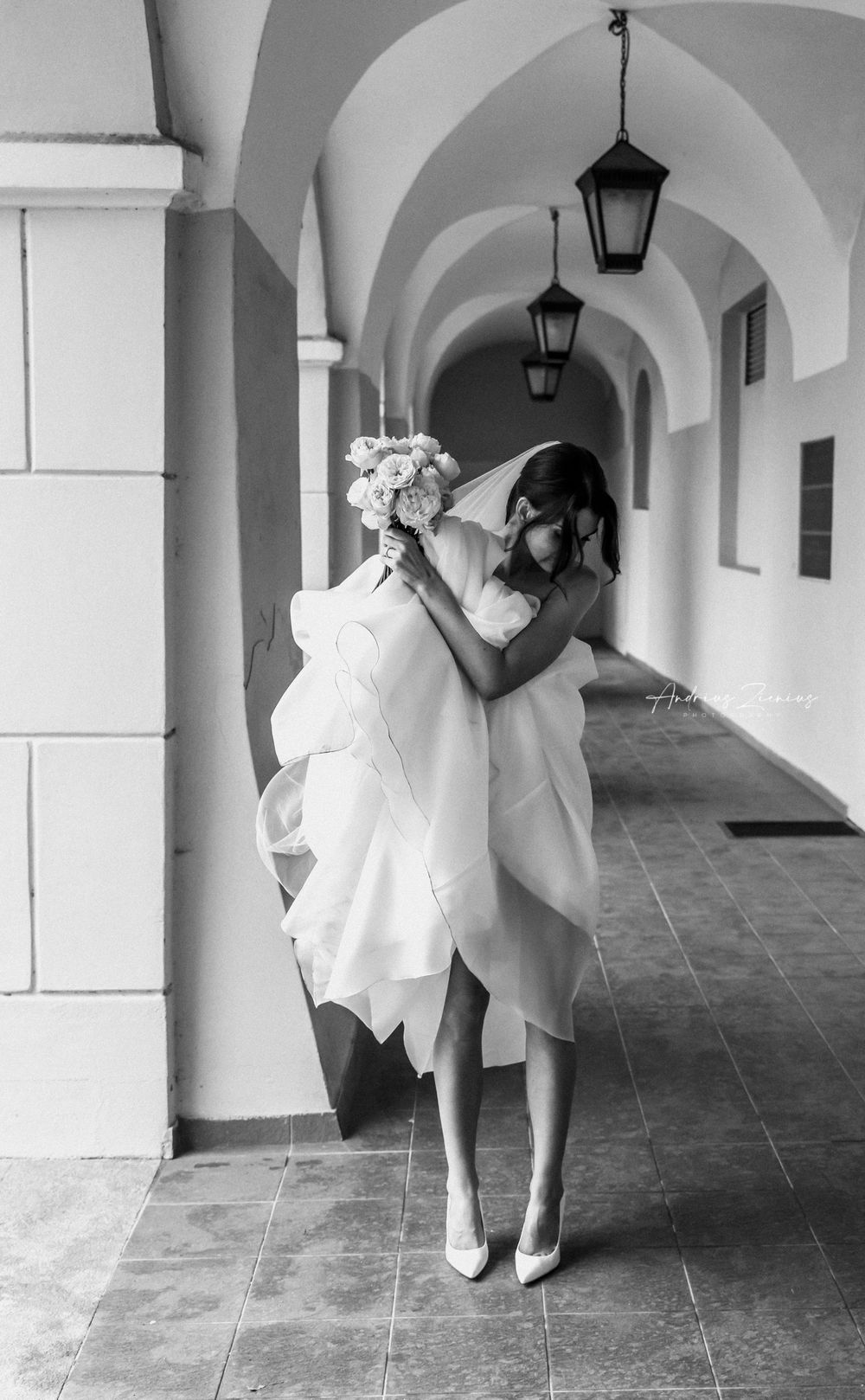 Bride poses elegantly in arched corridor with hanging lanterns in black and white.
