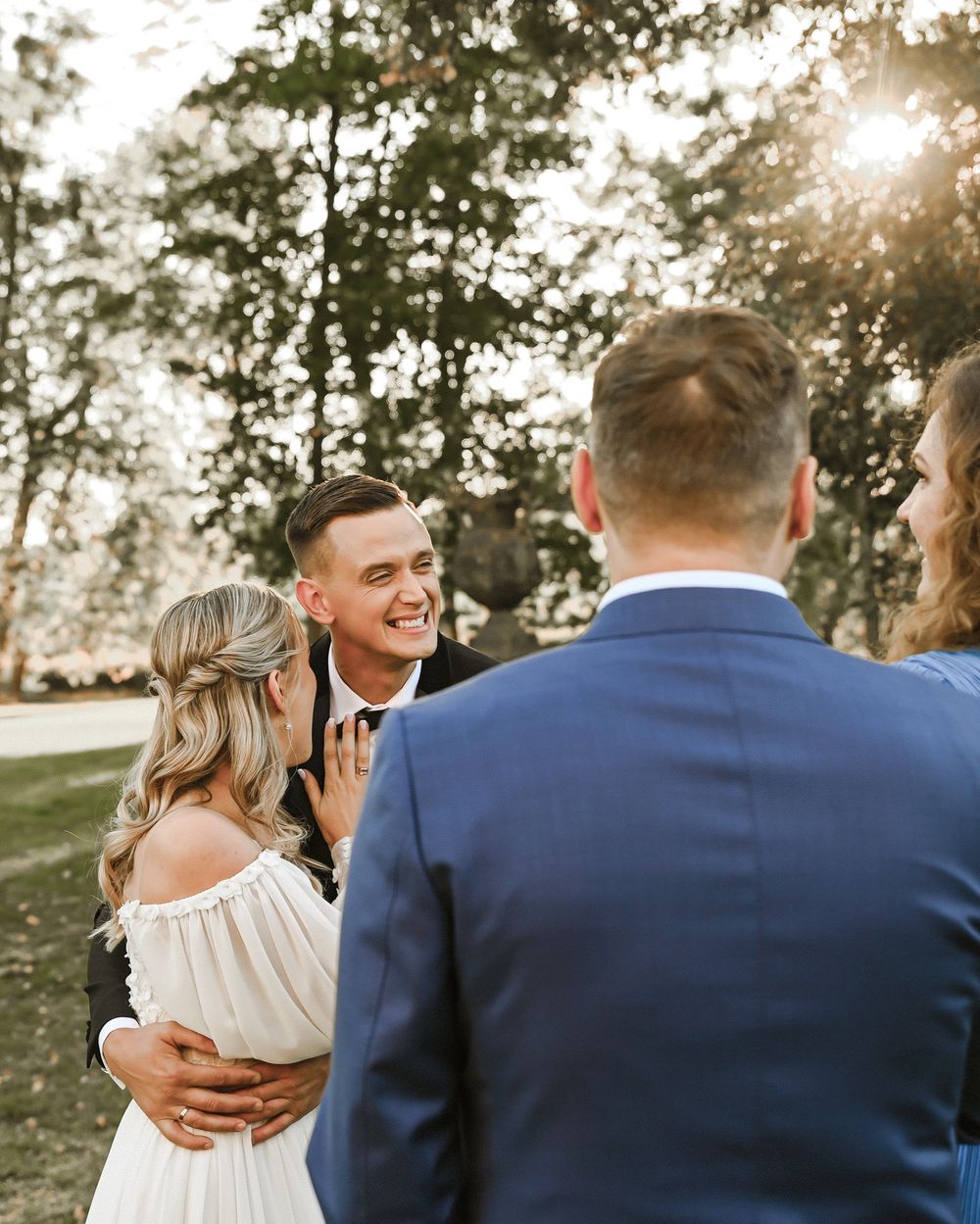 A romantic outdoor wedding ceremony takes place at golden hour with sunlight filtering through the trees.