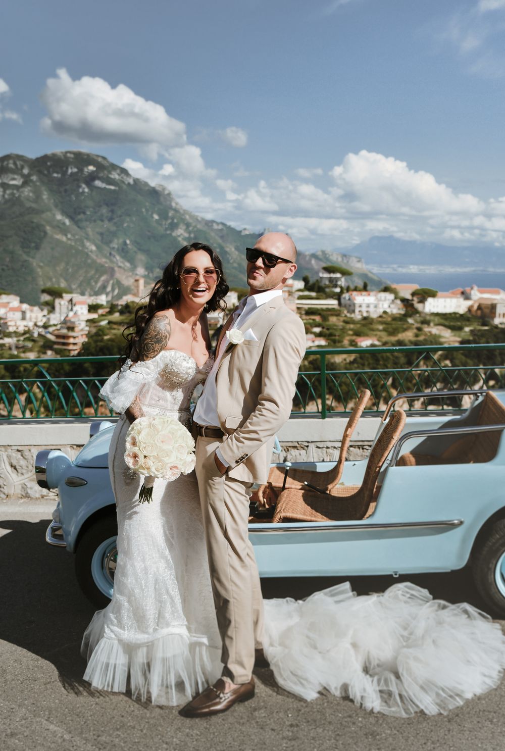 A couple poses with their vintage car during their wedding with stunning coastal mountains in the background.