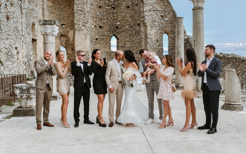 Wedding party gathers for group photos against stone wall backdrop at elegant venue.