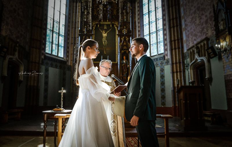 Wedding ceremony takes place in gothic church with stained glass windows.