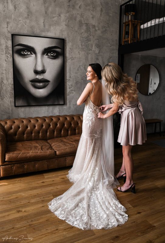 Elegant wedding dress with intricate lace train displayed in modern industrial space with leather couch.