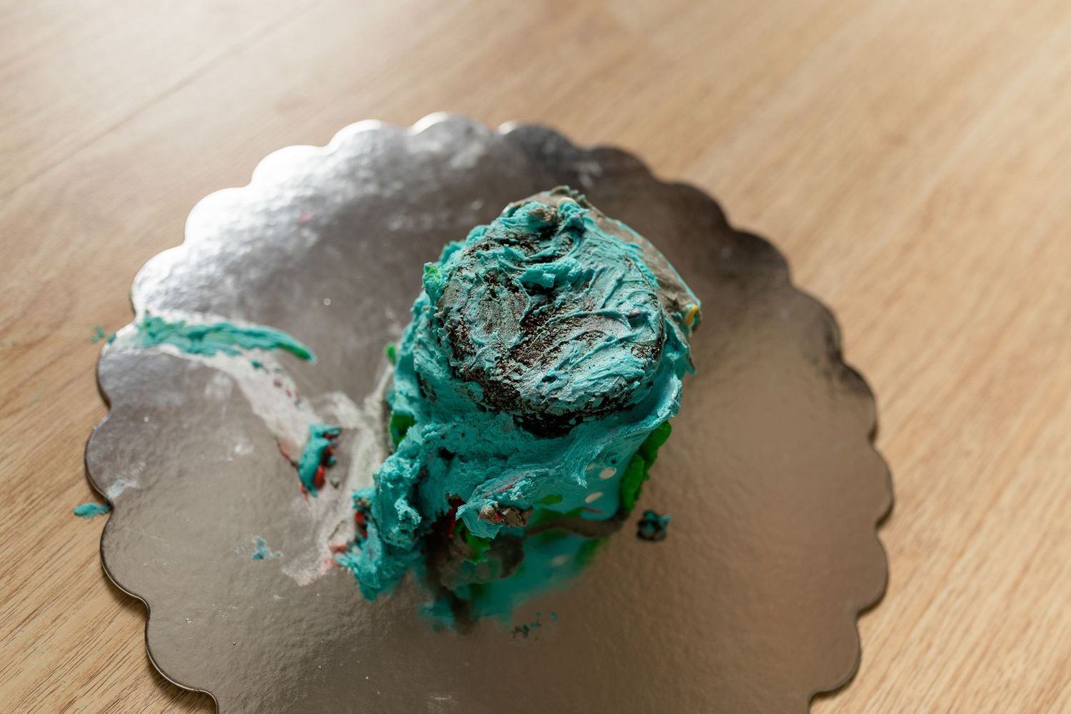 A smashed turquoise colored cake or frosting smear on a silver cake plate.
