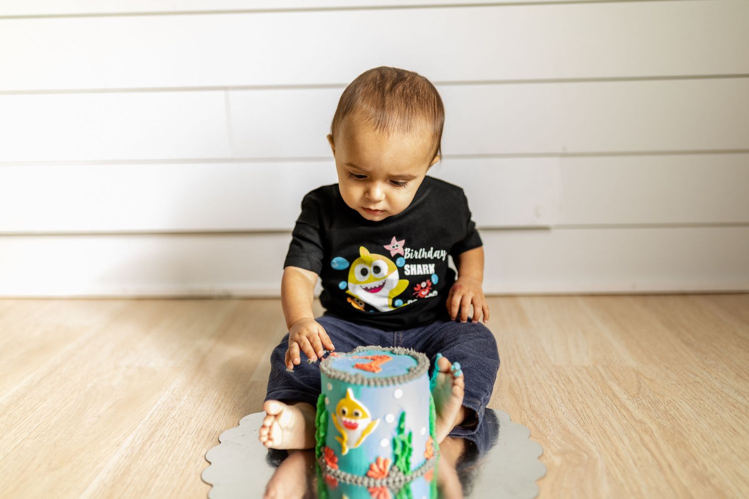 Small child interacting with a decorated teal container on hardwood flooring.