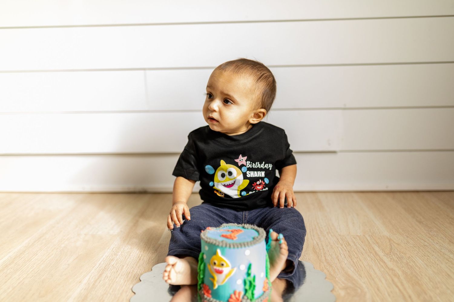Baby sitting on wooden floor examining a decorated teal cylinder.
