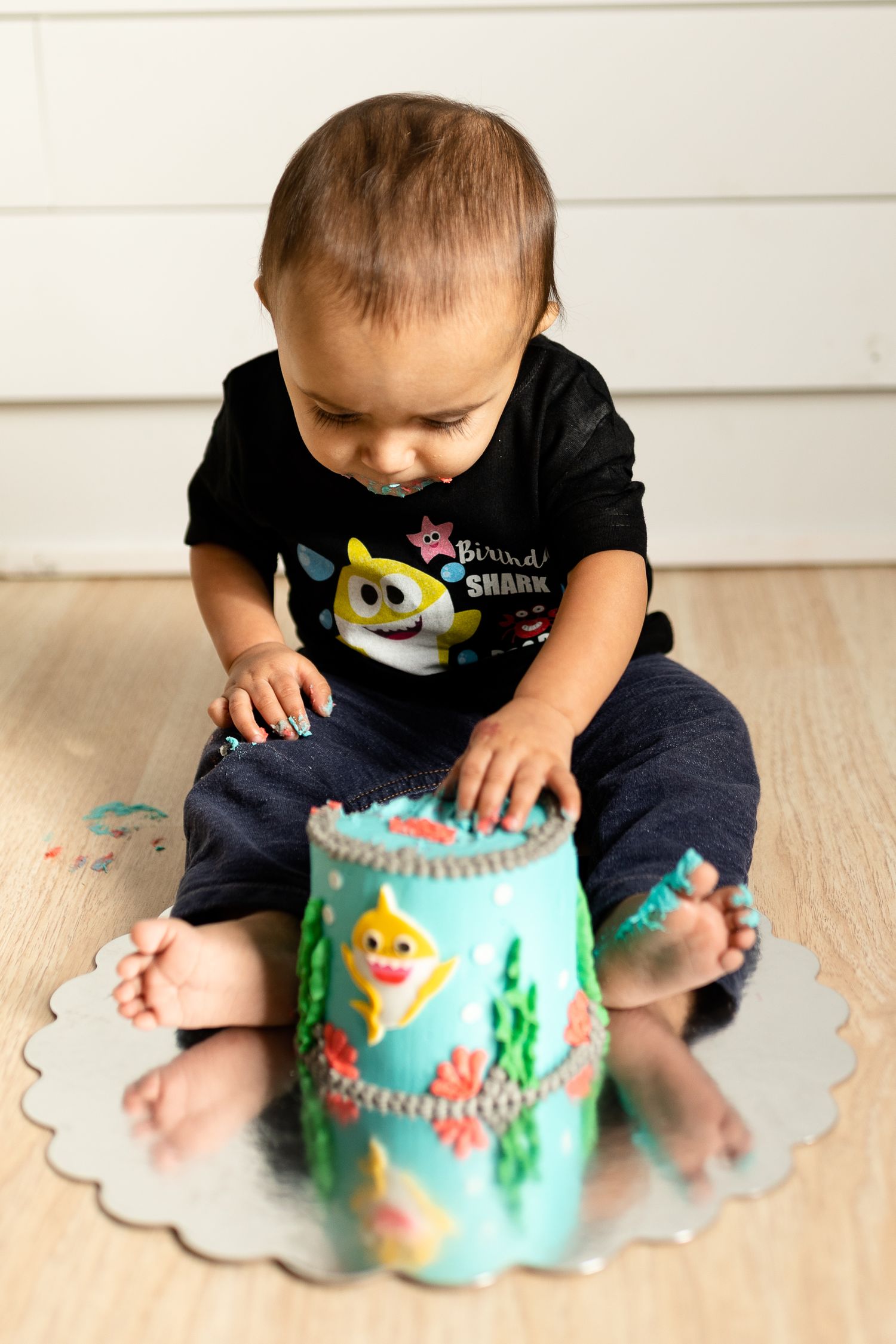 Small child in cartoon graphic t-shirt examining decorated teal container on wooden floor.