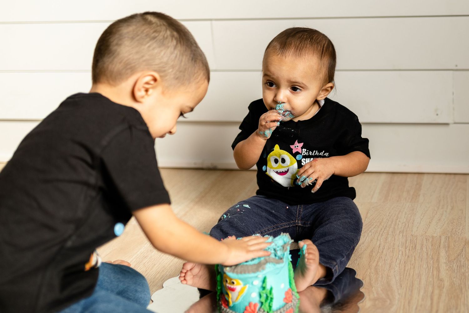 Two children playing together with a turquoise toy on a light wooden floor.