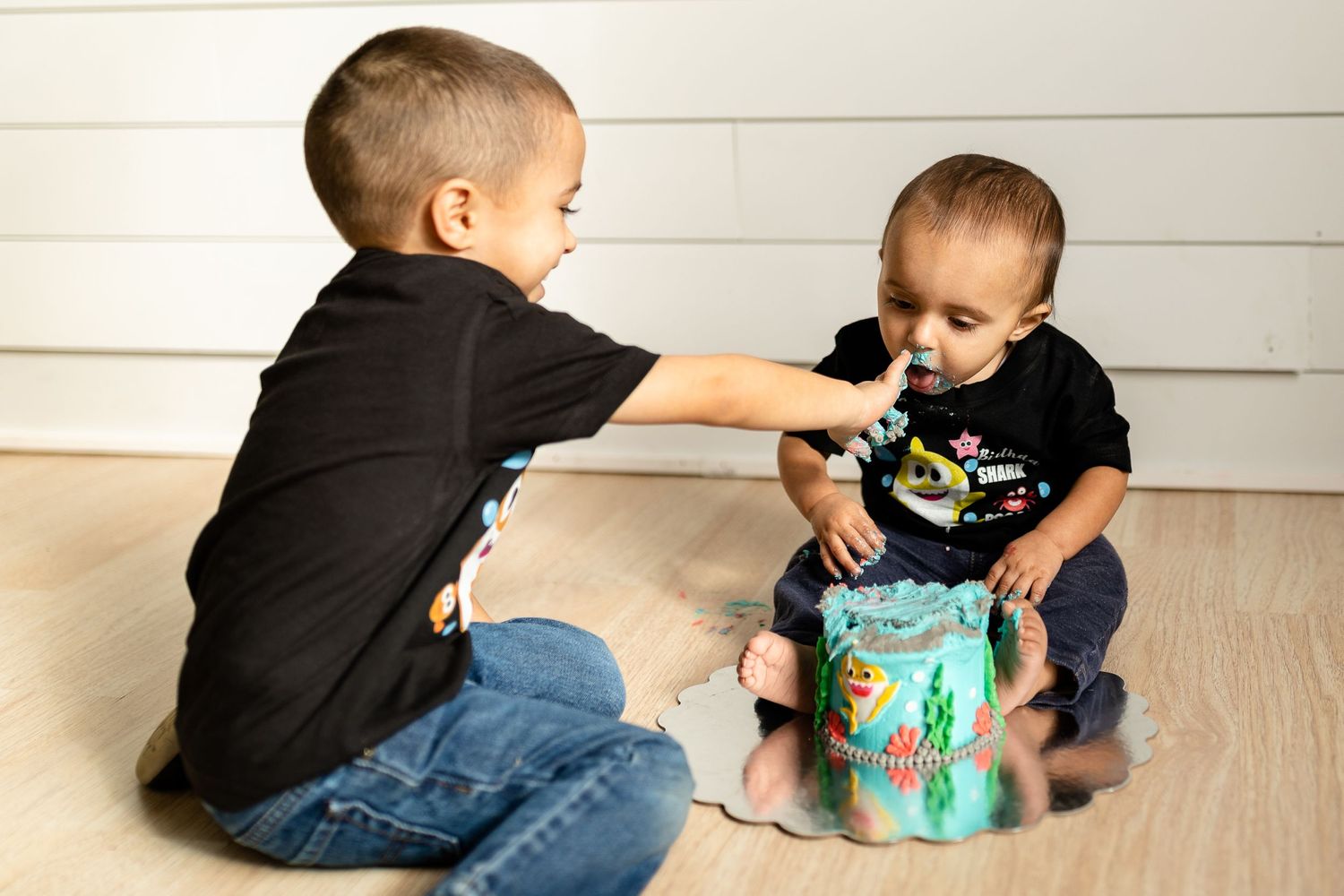 Two kids engaged in playtime with a bright turquoise toy against white shiplap walls.
