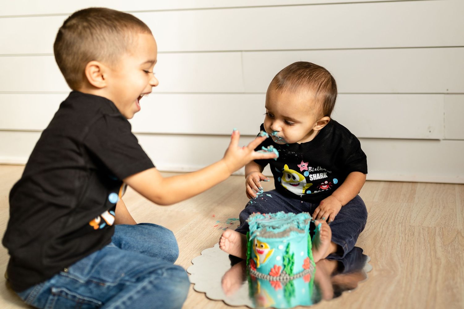 Young children interacting with turquoise colored toy on wooden flooring.